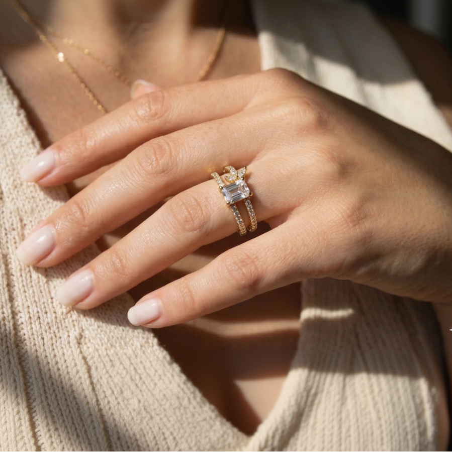 Close-up of a hand wearing a gold ring with a diamond on a blurred background