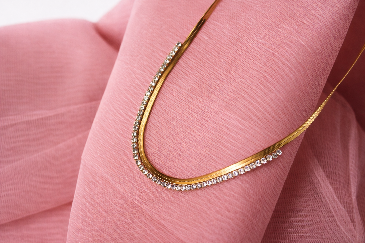 Gold necklace with small diamonds on a pink fabric background