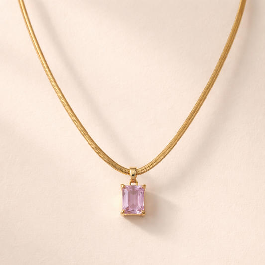 Gold necklace with a pink gemstone pendant on a beige background