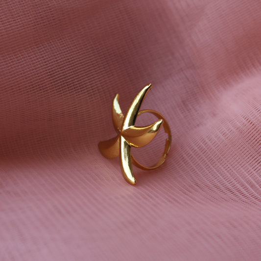 Gold ring with a leaf design on a pink fabric background