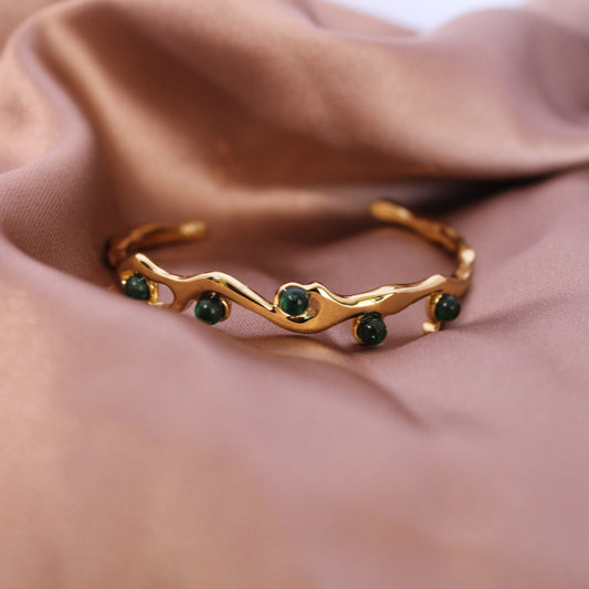 Gold ring with green gemstones on a soft brown fabric background