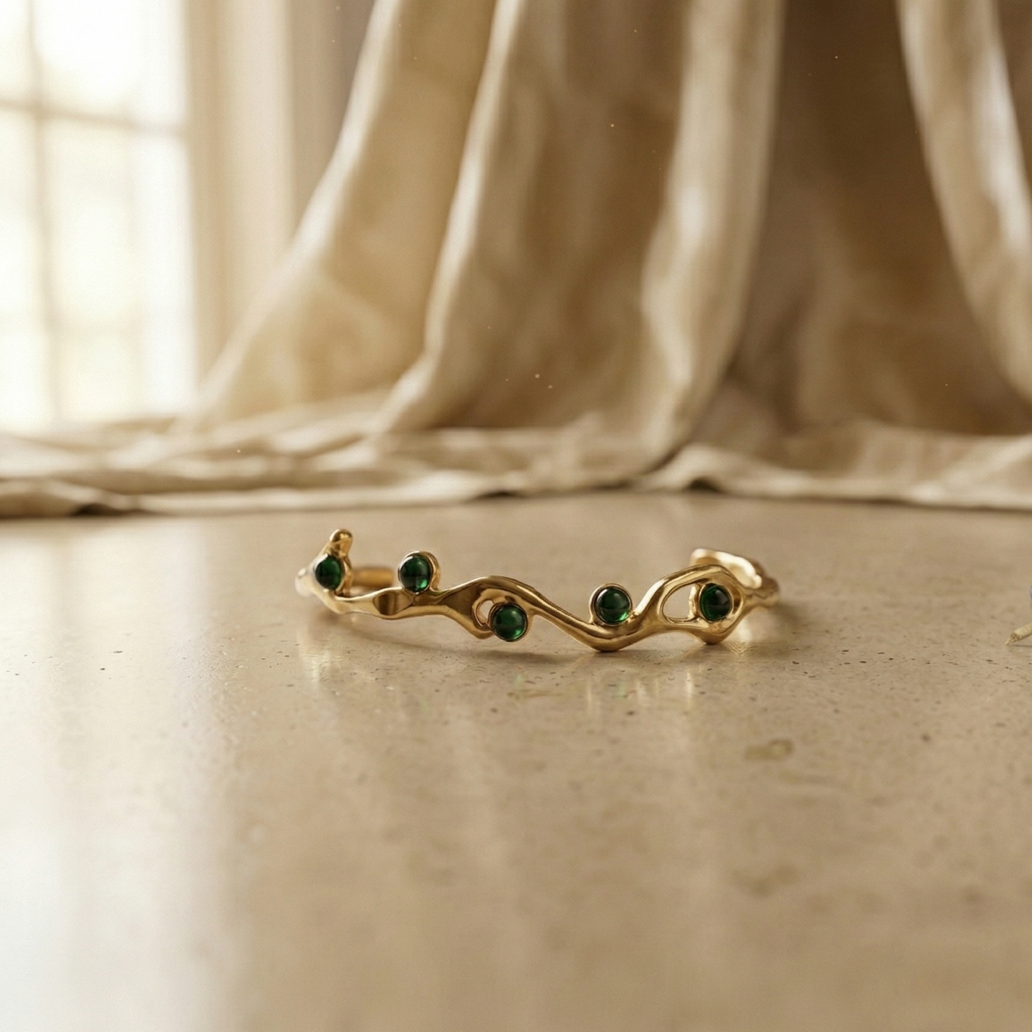 Gold ring with green gemstones on a beige surface