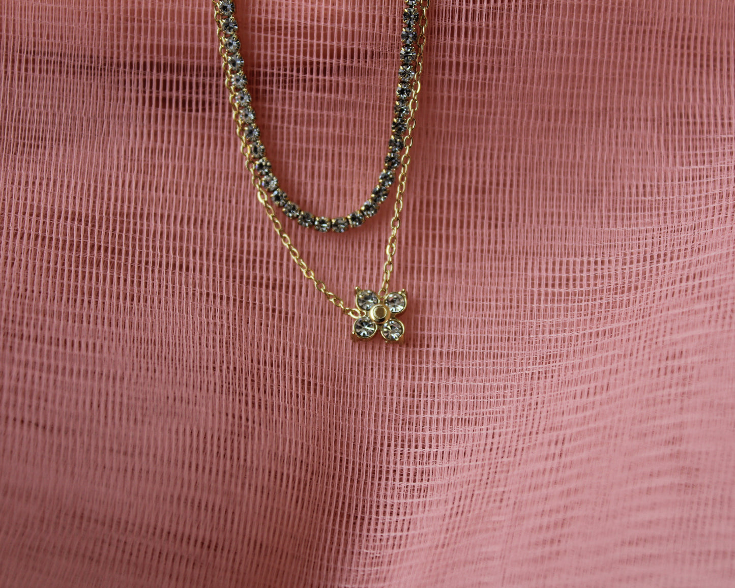 Two gold necklaces with green gemstones on a pink textured fabric background