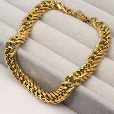 A thick gold-toned curb chain bracelet displayed on a light gray jewelry ring holder.