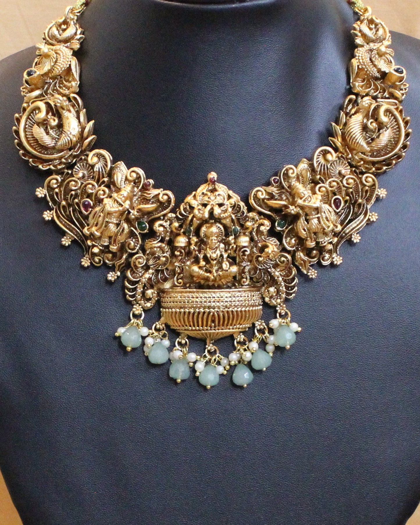 Gold necklace and earrings on a black stand with a beige curtain background