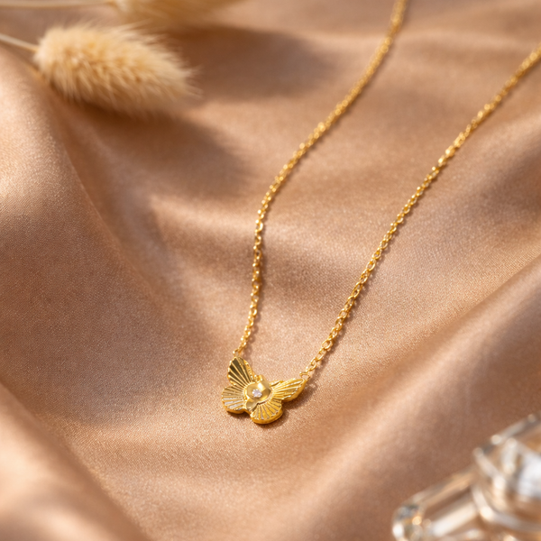 Gold necklace with a butterfly pendant on a soft pink fabric background