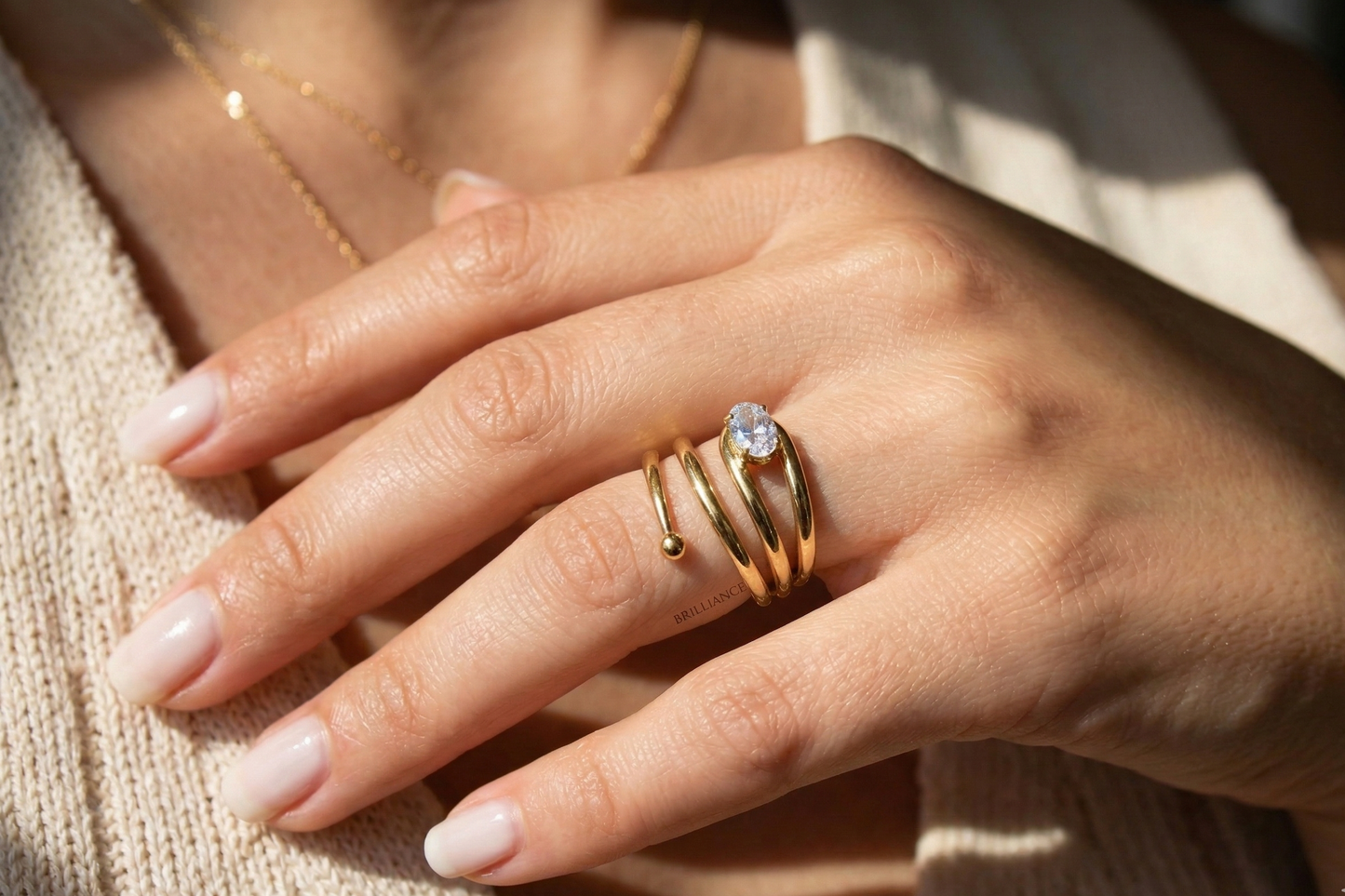 Close-up of a hand wearing multiple gold rings with a diamond on a light background
