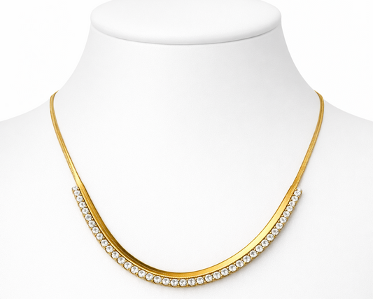 Gold necklace with clear stones on a mannequin bust against a white background
