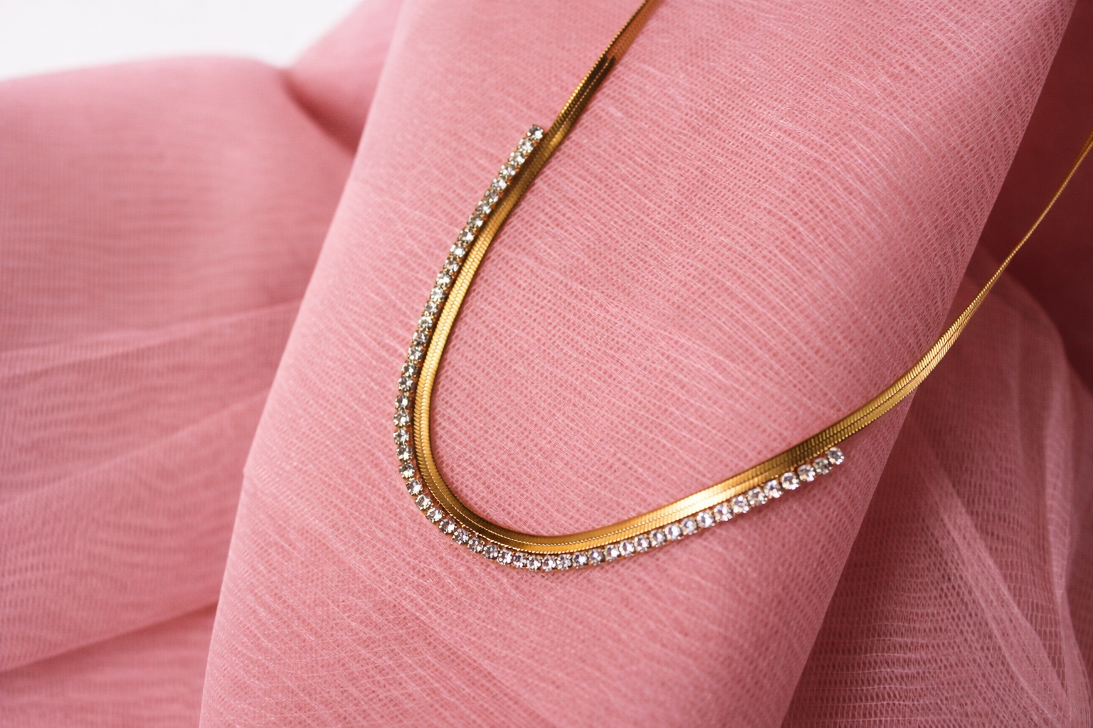 Gold necklace with small diamonds on a pink fabric background