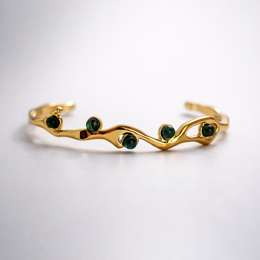 Gold bracelet with green gemstones on a white background
