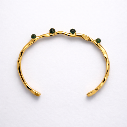Gold bracelet with green stones on a white background
