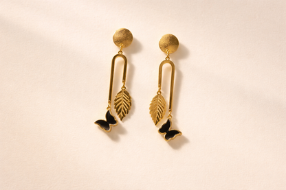Gold earrings with leaf and butterfly designs on a beige background