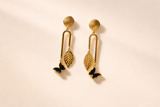 Gold earrings with leaf and butterfly designs on a beige background