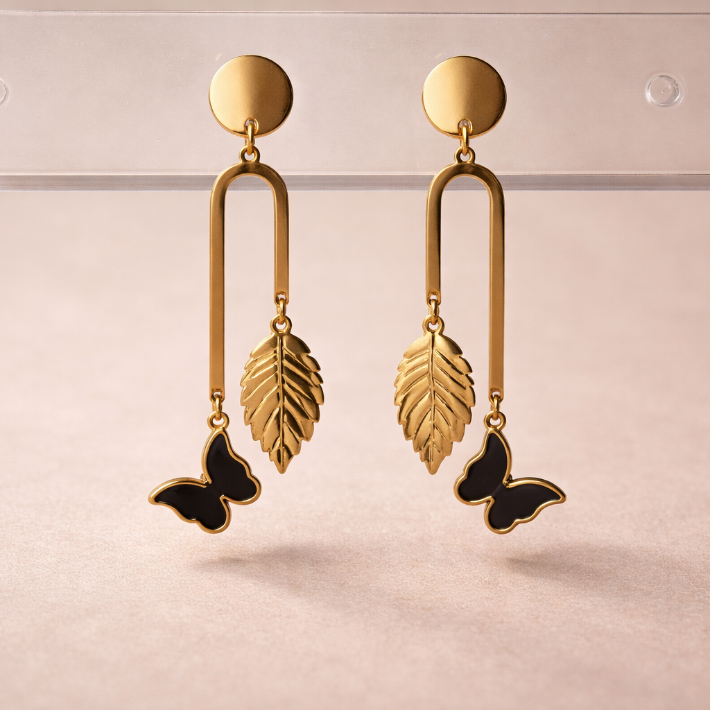Gold earrings with leaf and butterfly designs on a light pink background