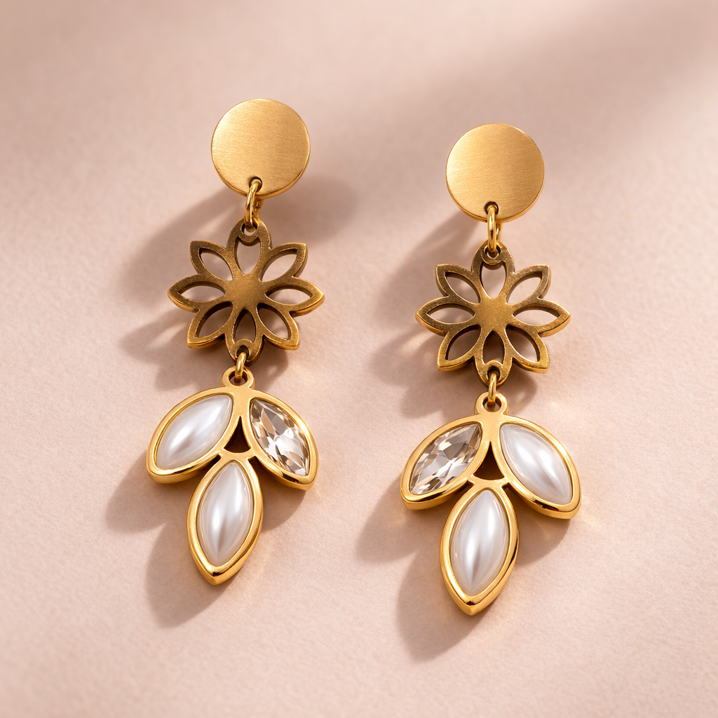 Gold earrings with floral designs and white stones on a pink background