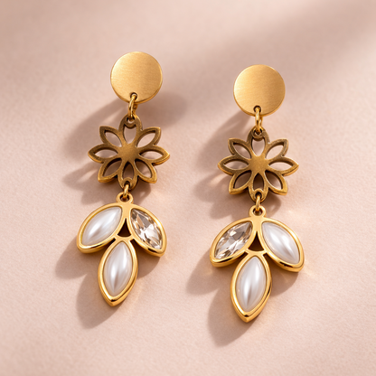 Gold earrings with floral designs and white stones on a pink background