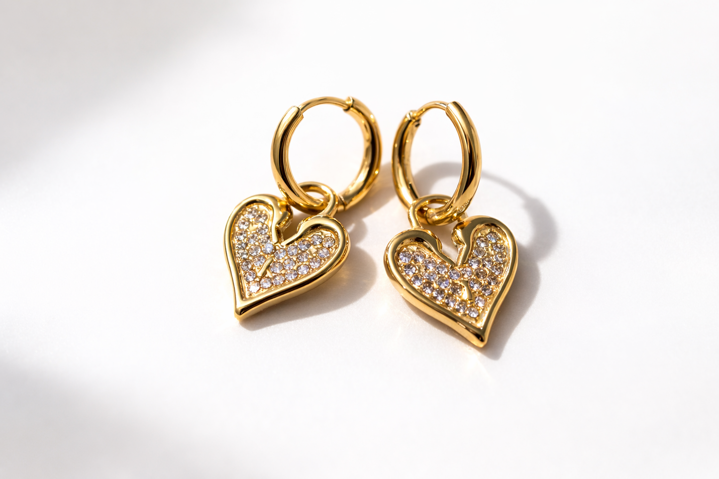 Gold heart-shaped earrings with embedded stones on a white background