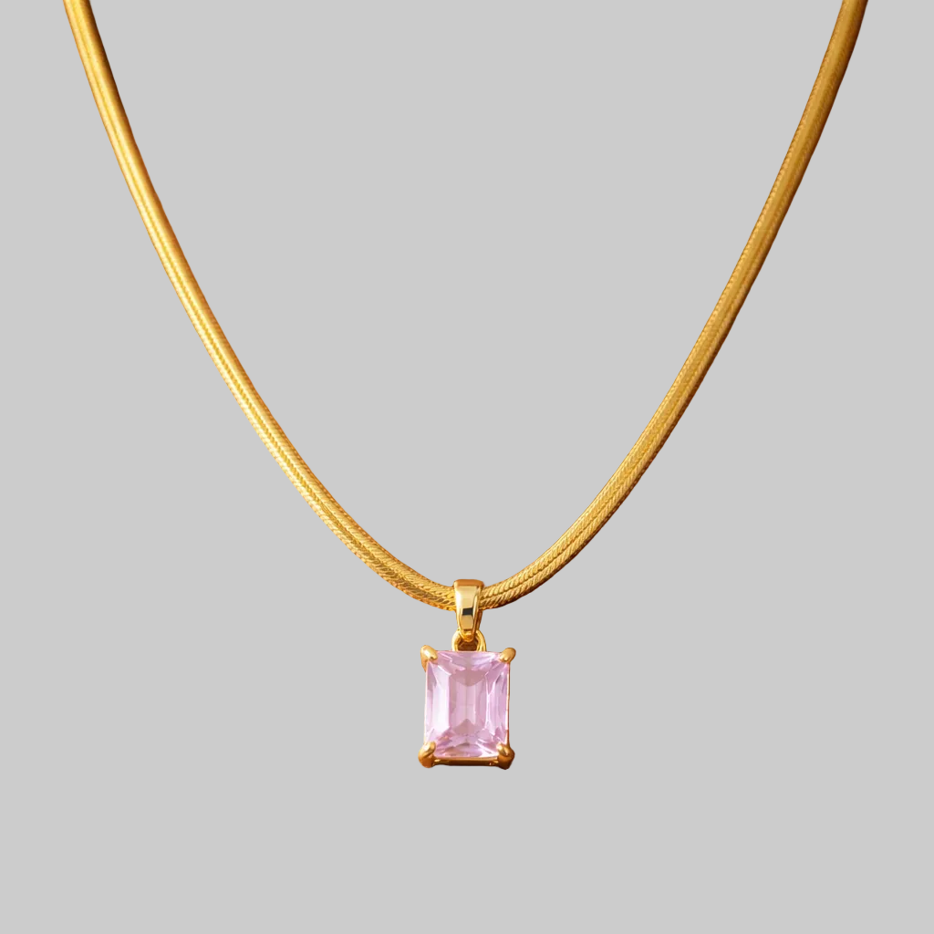 Gold necklace with a pink gemstone pendant on a wooden surface