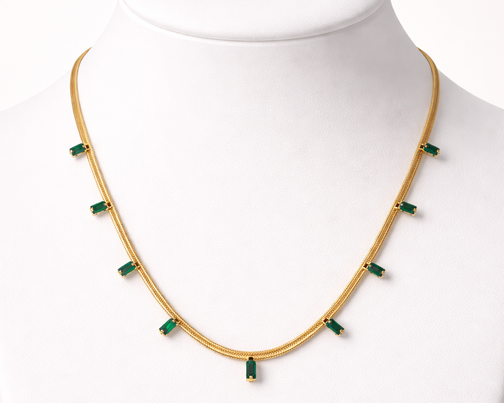 Gold necklace with green beads on a mannequin against a white background