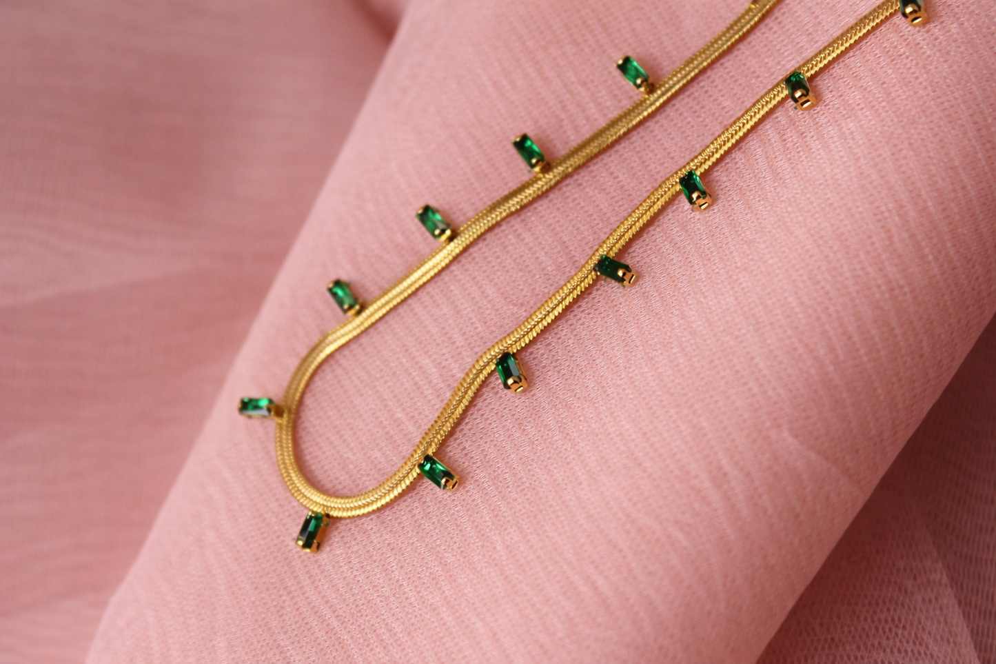 Gold jewelry with green gemstones on a pink fabric background