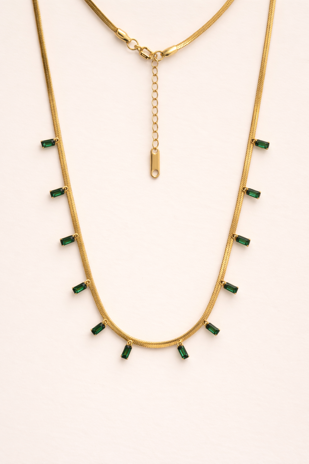 Gold necklace with green gemstones on a white background