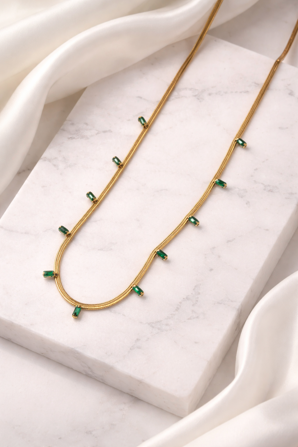 Gold necklace with green gemstones on a marble surface