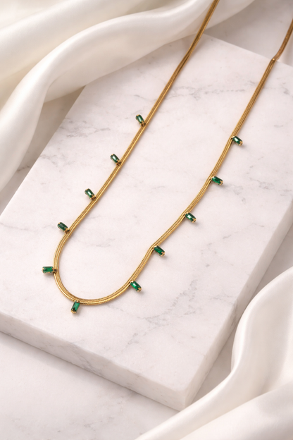 Gold necklace with green gemstones on a marble surface