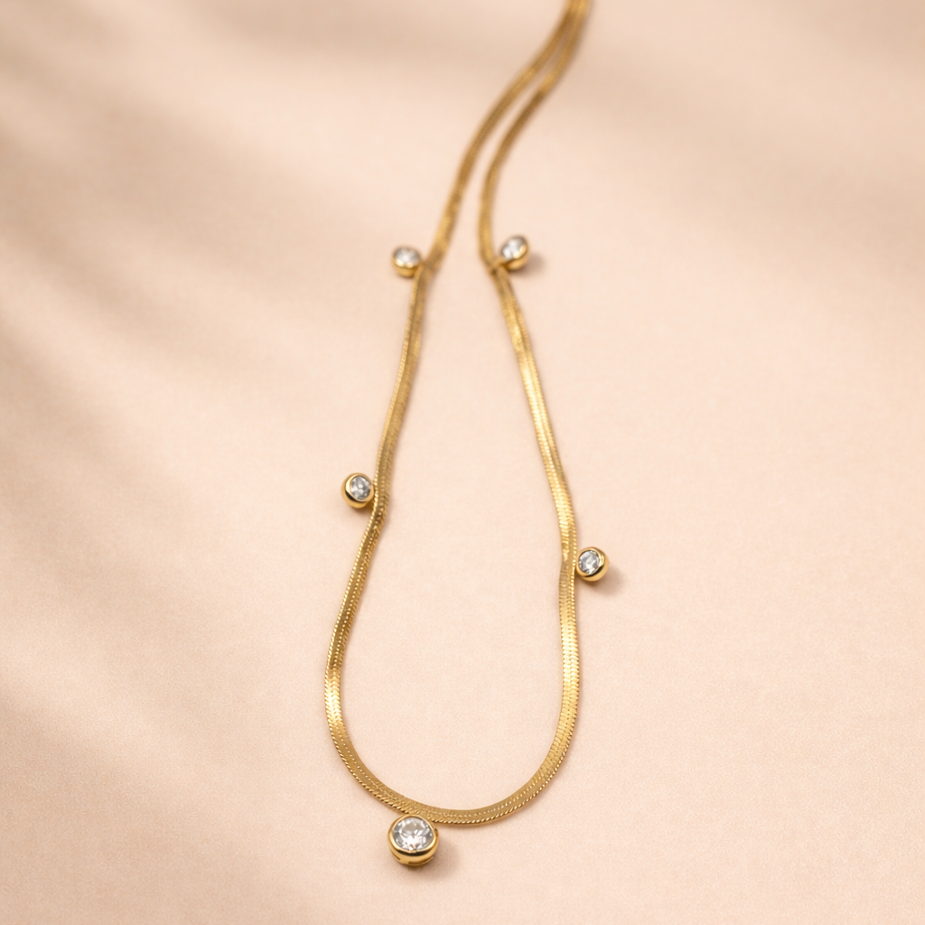 Gold necklace with small round beads on a soft pink background