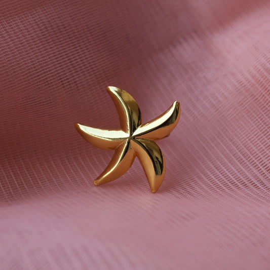 Gold ring with a leaf design on a pink fabric background