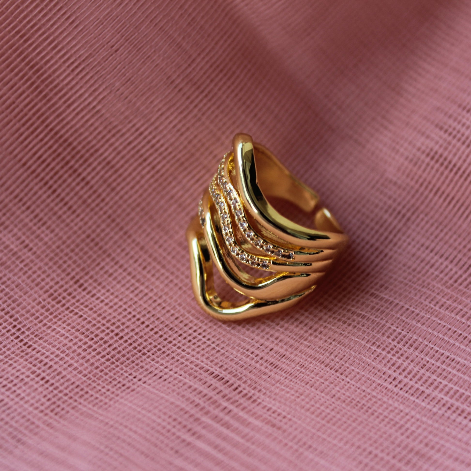 Gold ring with a textured design on a pink fabric background