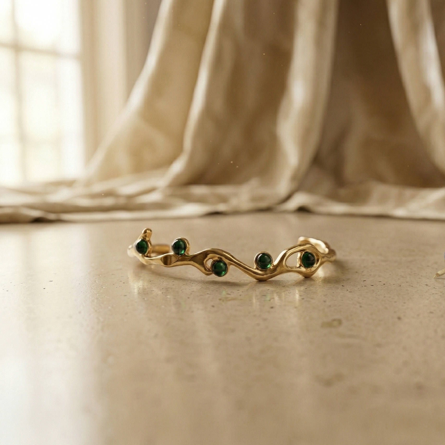 Gold ring with green gemstones on a beige surface