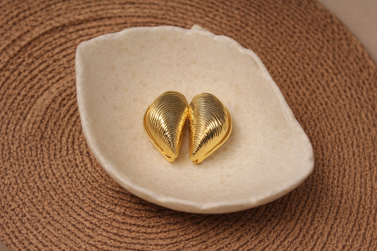 Gold shell-shaped earrings on a white dish with a brown textured background