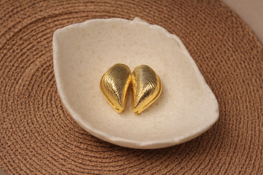 Gold shell-shaped earrings on a white dish with a brown textured background