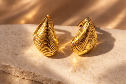 Pair of gold earrings on a marble surface with a soft background