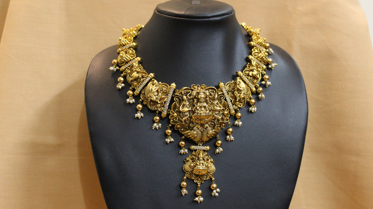Gold necklace on a black mannequin against a beige background