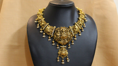 Gold necklace on a black mannequin against a beige background