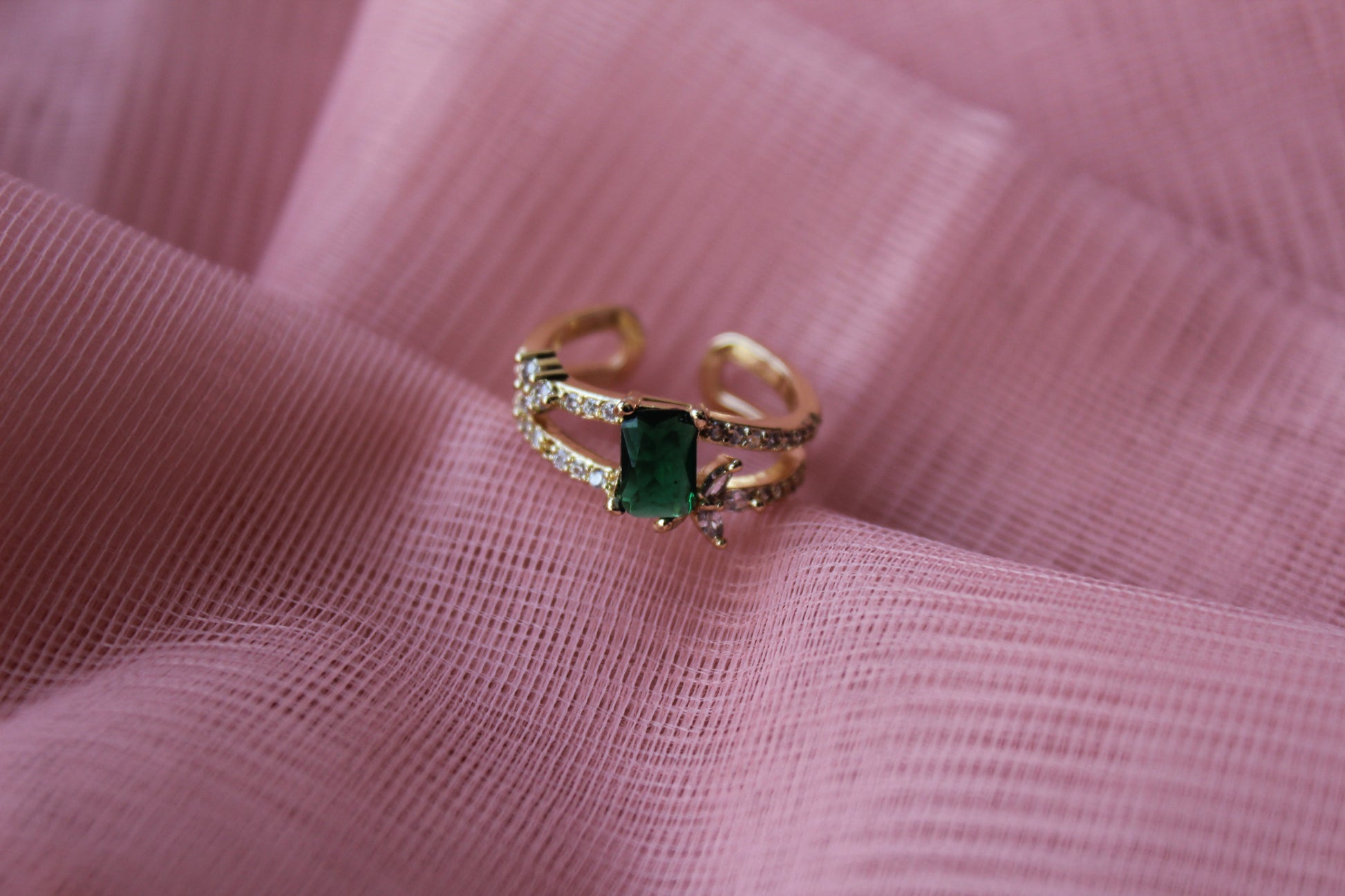Gold ring with a green gemstone on pink fabric