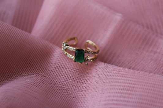 Gold ring with a green gemstone on pink fabric
