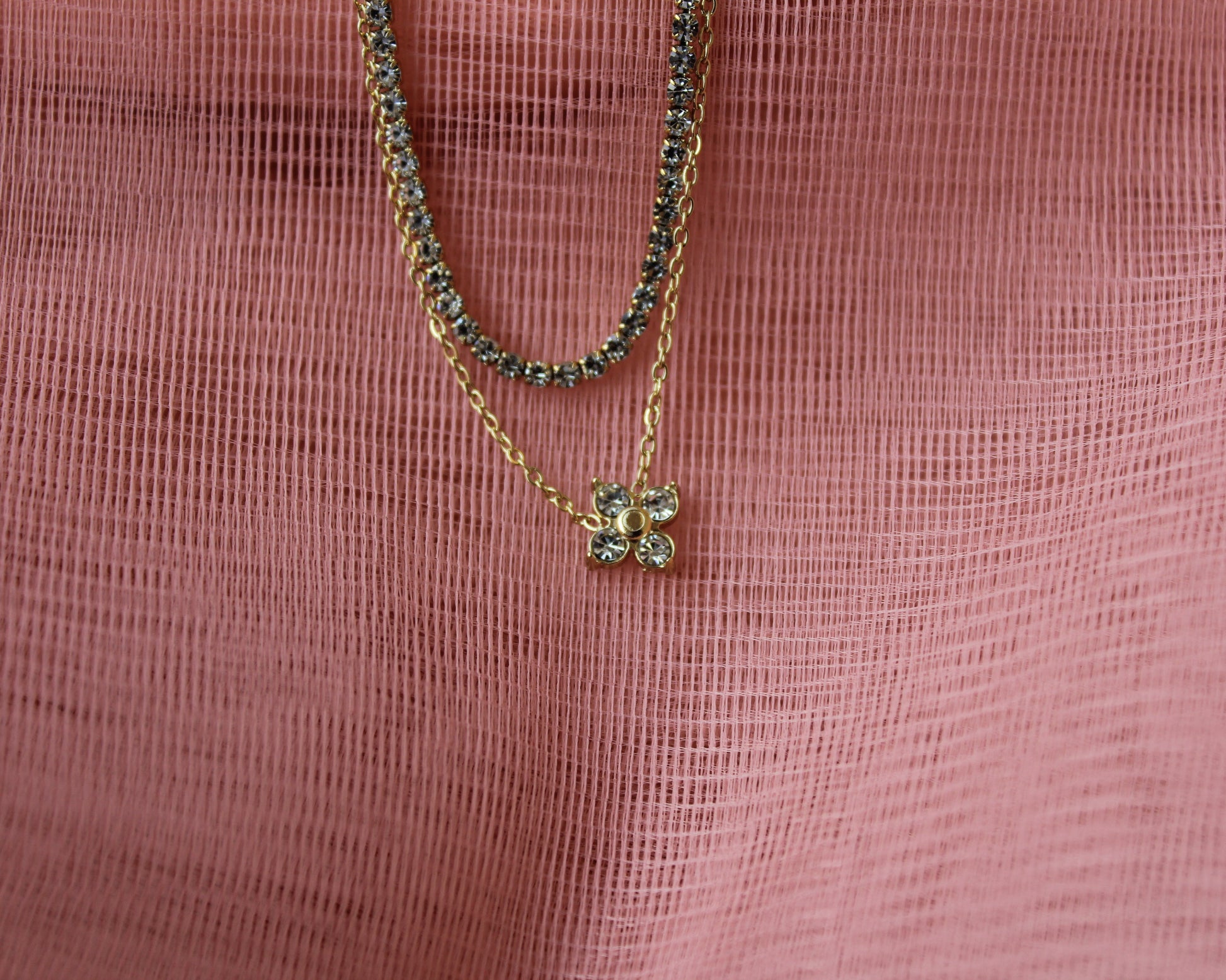 Two gold necklaces with green gemstones on a pink textured fabric background