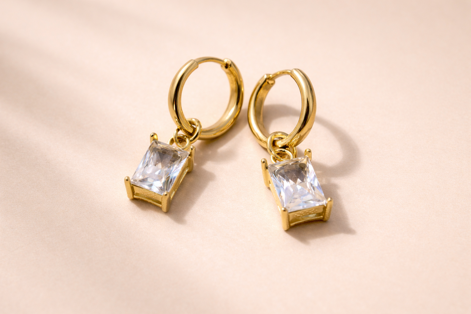 Gold hoop earrings with clear gemstones on a beige background