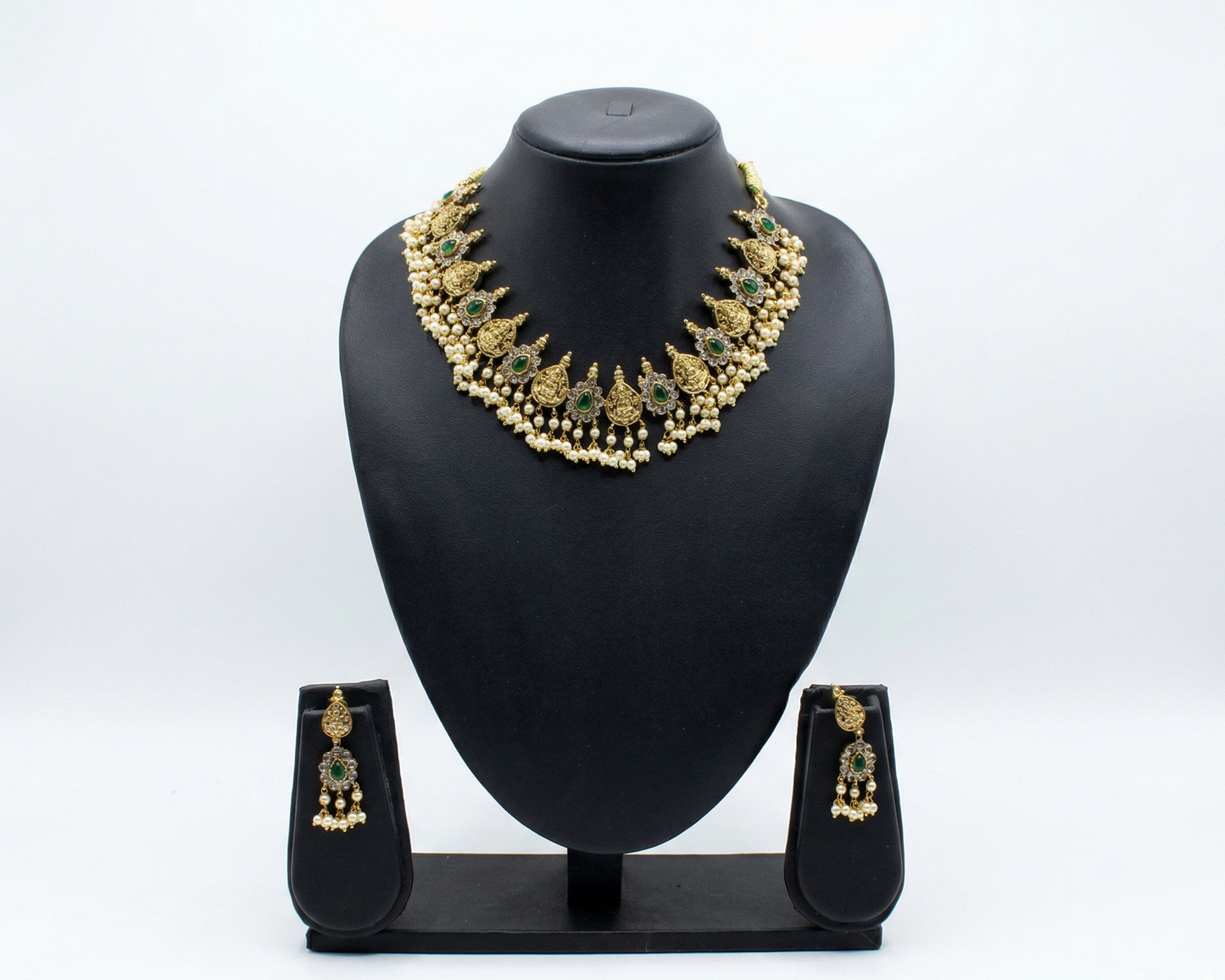 Gold necklace and earrings set on a black mannequin bust against a white background