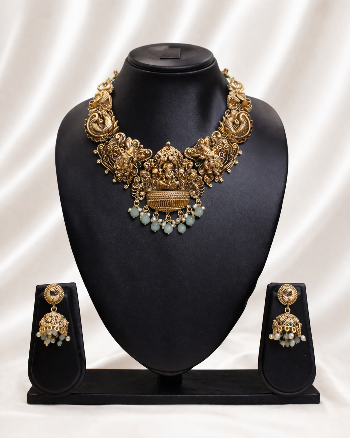 Gold necklace and earrings set on a black mannequin bust with a white background
