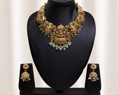 Gold necklace and earrings set on a black stand with a white background
