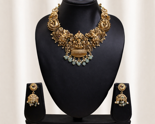 Gold necklace and earrings set on a black stand with a white background