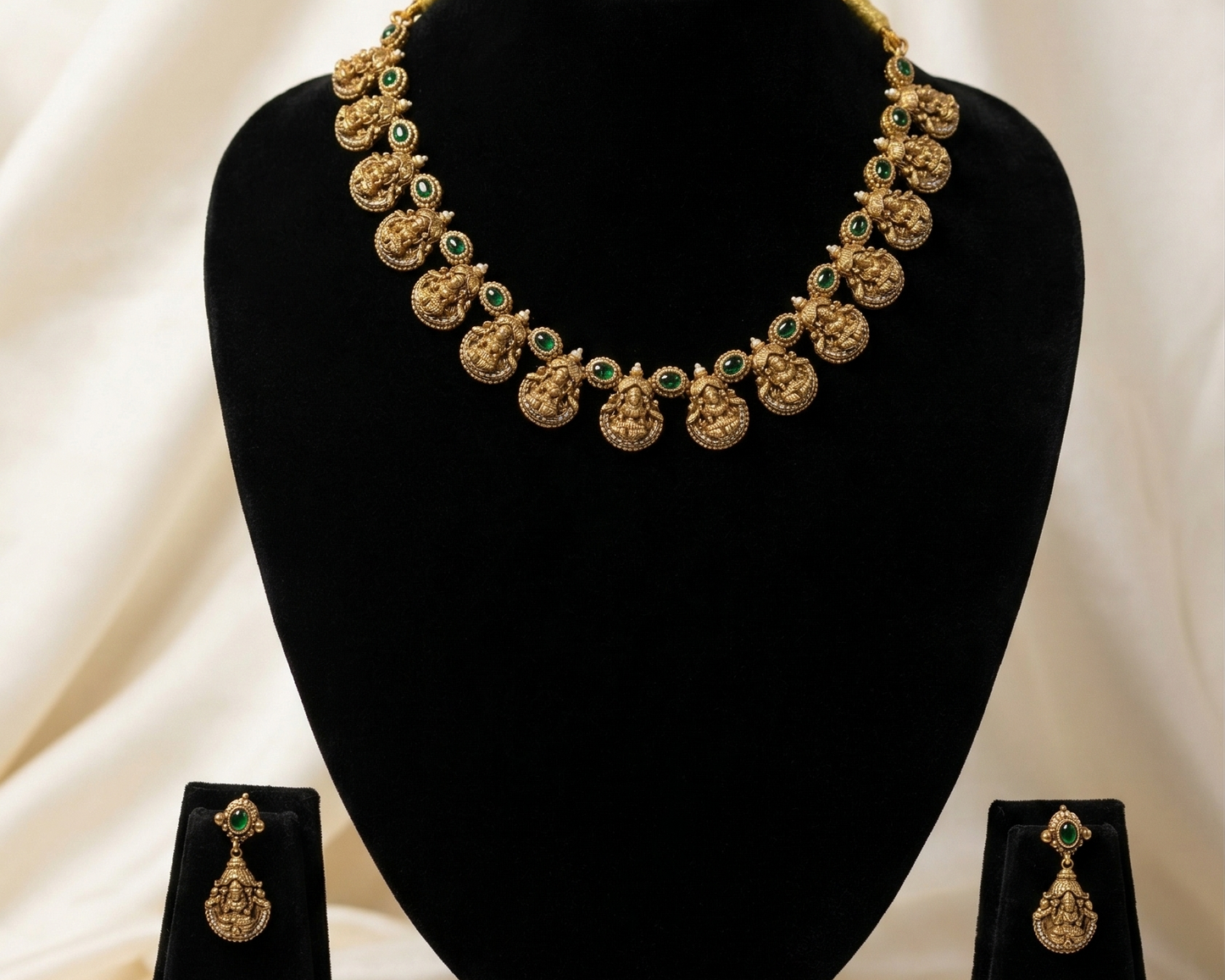 Gold necklace and earrings on a black stand against a white background