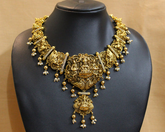 Gold necklace on a black mannequin against a beige background