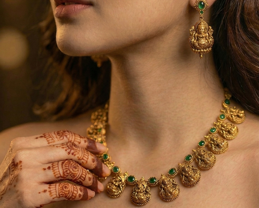 Woman wearing gold jewelry with green gemstones, including a necklace and earrings.